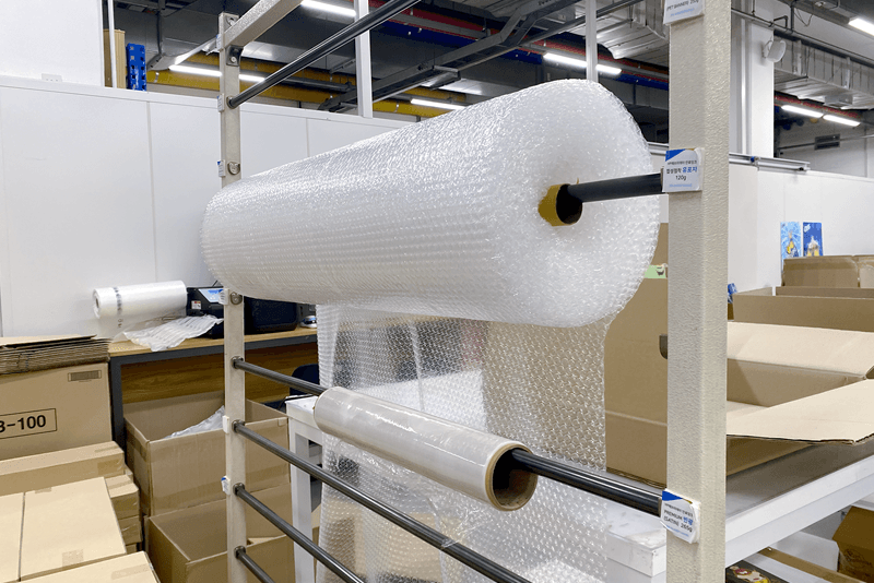 2_포장배송_10_킨코스 포장 구역 내 버블랩과 스트레치 필름이 걸려 있는 포장 자재대, 보호 포장을 위한 자재 관리 시스템