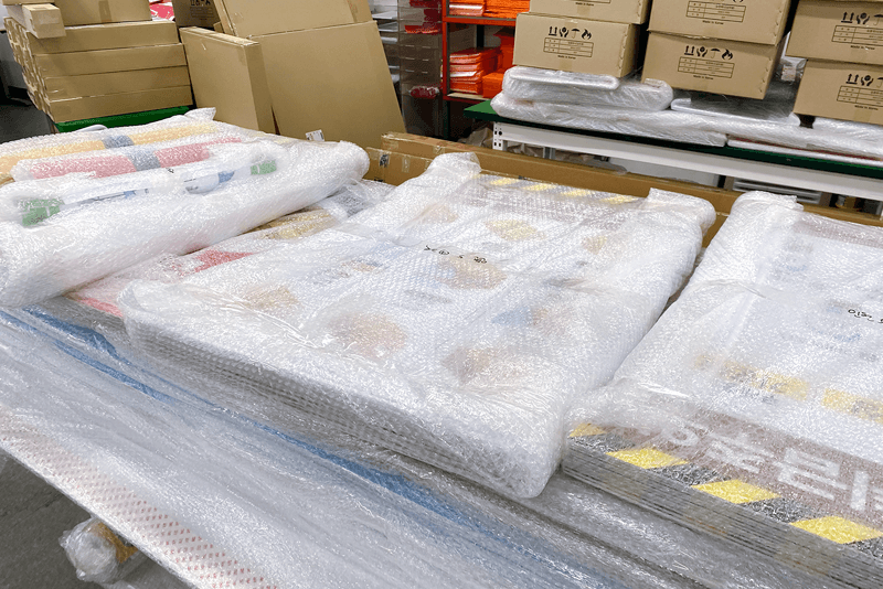 2_포장배송_4_버블랩으로 보호 포장된 POP와 인쇄물이 포장대 위에 놓여 있는 모습, 파손 방지를 위한 완충 포장 과정