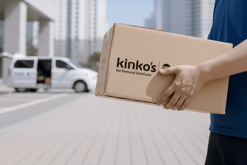 2_포장배송_9_킨코스 직원이 로고가 인쇄된 박스를 들고 배송 차량 쪽으로 이동하는 장면, 고객사로 직접 납품하는 마지막 단계
